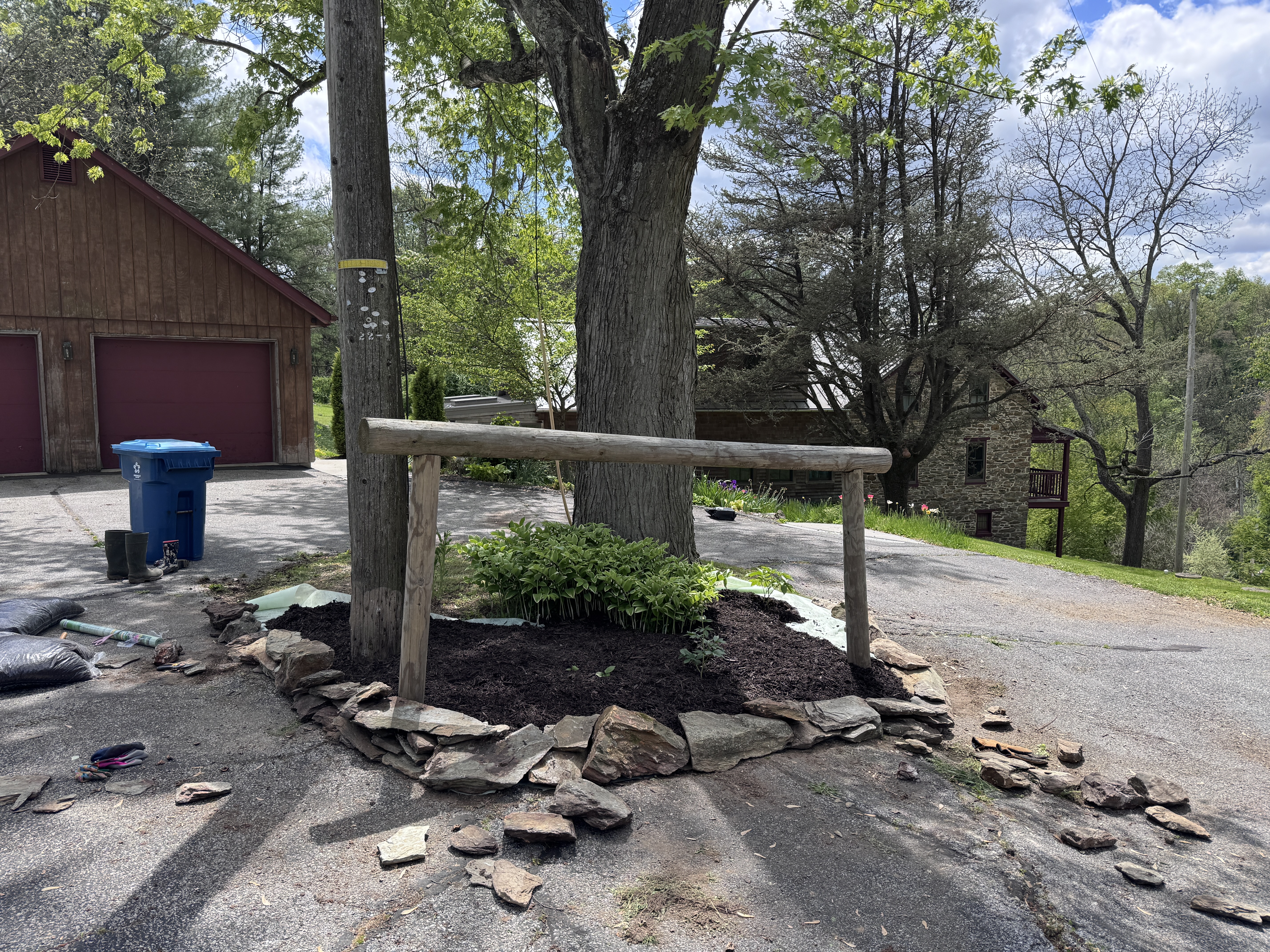 Stone wall taking shape around the island, flat fieldstones laid in a ring, stones still scattered on the driveway